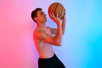 Young athletic man, with basketball, posing on background with neon lights