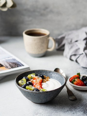 Delicious breakfast - the cup of coffee and granola with yogurt and berries and open magazine on the table. Copy space.