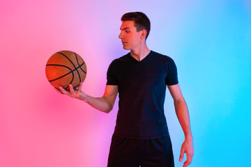 Young athletic man, with basketball, posing on background with neon lights