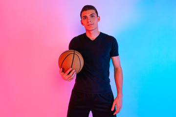 Naklejka premium Young athletic man, with basketball, posing on background with neon lights