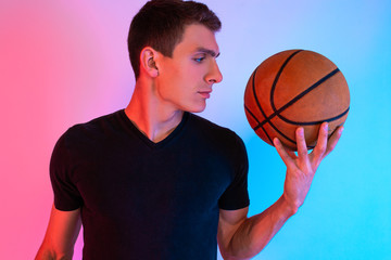 Young athletic man, with basketball, posing on background with neon lights