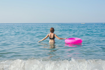 Young woman with pink swimming ring is swimming in the sea in sunny day. Summer vacation concept.