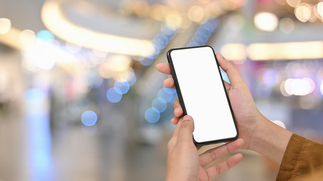 Close-up image of woman hand while using/holding a white blank screen smartphone over the blurred supermarket background.