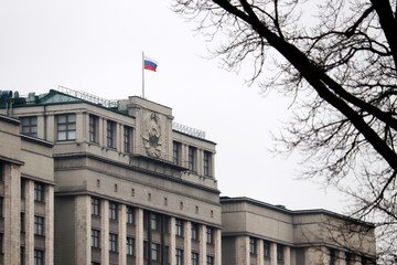 Fototapeta na wymiar Parliament building in Moscow and bare tree branches against cloudy sky, selective focus. Russian authority, facade of State Duma of Russia with flag