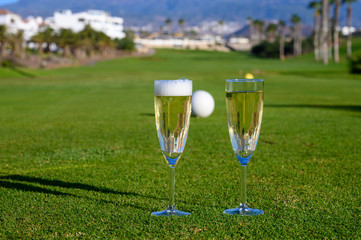 Two glasses with  bubbles white champagne or cava wine served on green golf club grass with mountains view during golf competition event or celebration