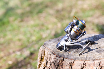 silver fishing reel close up on a stump against a sunny nature landscape with copy space