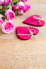 Small pink roses and two red wooden hearts on a background of unpainted and untreated boards. Valentine's day composition, selective focus.