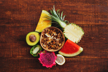 Tropic fresh summer fruits and granola seeds on brown wooden background, healthy organic super food on table, detox nutrition for health care, top view, copy space