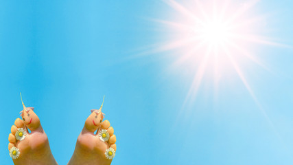 Spring summer background - Naked children's feet with smileys and blooming flowers isolated on blue sky with sun during the day