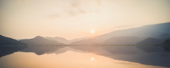 Fototapeta na wymiar Mountain lake with perfect reflection at sunrise. beautiful landscape with pink pastel sky with hills on background and reflected in water. Nature lake landscape