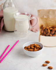Obraz na płótnie Canvas A handful of almonds in close-up, next to a package of nuts with space for text and logo. In the background, a mug and a bottle of milk.