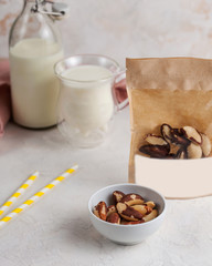 A handful of Brazil nuts in close-up, next to a package of nuts with space for text and logo. In the background, a mug and a bottle of milk.