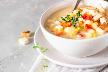 Bowl of homemade corn chowder soup with potatoes, carrots, red bell pepper and croutons on a light grey stone background. Delicious cozy first course, comfort food.