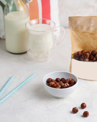 A handful of hazelnuts, hazelnuts close-up, next to a package of nuts with space for text and logo. In the background, a mug and a bottle of milk.