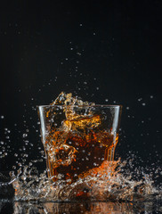 Glass of whiskey with splash isolated on black background