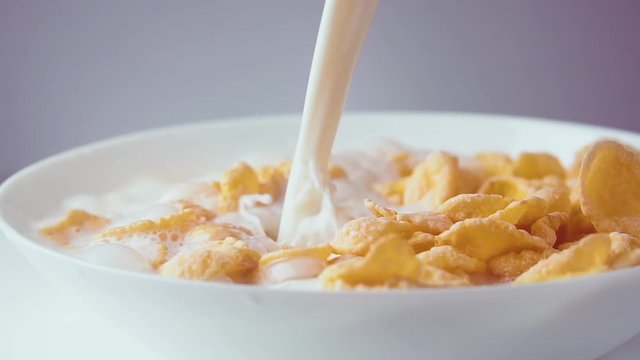 Milk pouring into bowl of cornflakes, slow motion. Healthy breakfast of cereal with milk, close up.