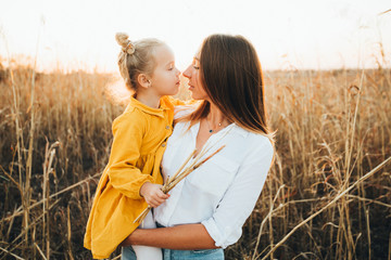 Mom and daughter are hugging and smiling while standing in a beautiful summer field.