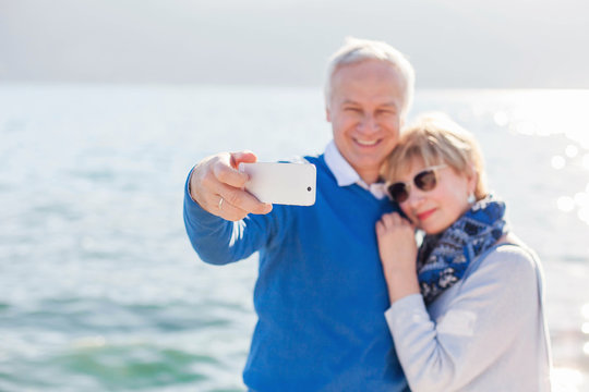 Senior couple take photo selfie at sea beach outdoor. Happy man and woman using mobile phone. Travellers enjoying retirement and traveling. Lifestyle moments. Active seniority.