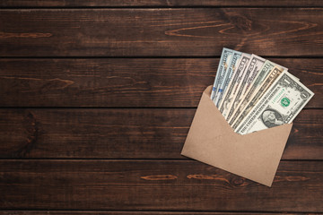 Close-up kraft paper envelope with one hundred dollar bills on brown wooden background, bundle of...