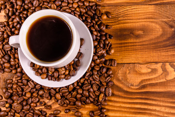 Cup of hot coffee and scattered coffee beans on wooden table. Top view
