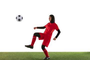 Arabian female soccer or football player isolated on white studio background. Young woman kicking the ball, training, practicing in motion and action. Concept of sport, hobby, healthy lifestyle.