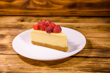 White plate with cheesecake New York and raspberries on wooden table