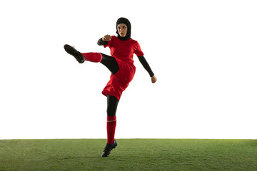 Fototapeta na wymiar Arabian female soccer or football player isolated on white studio background. Young woman kicking the ball, training, practicing in motion and action. Concept of sport, hobby, healthy lifestyle.