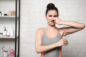 shocked woman plugging nose with hand while applying deodorant on underarm