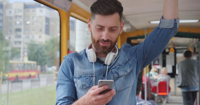 Young Handsome Bearded Man Using public Transport, Looking Happy and Pleasant. Chatting on his Mobile Phone. Search for popular songs and nice music at the App. Having Headphones