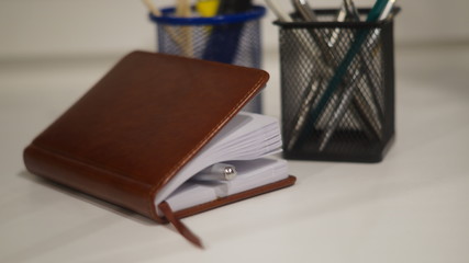 a brown diary and two stationery glasses with paint brushes and pens