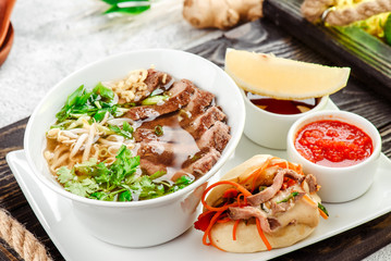 Asian noodle soup, ramen with beef, tofu, vegetables in white plate on a dark restik tray
