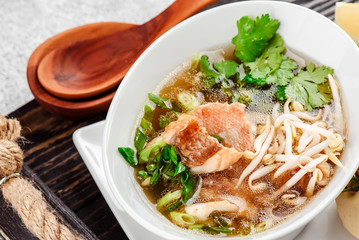 Asian noodle soup, ramen with fish, tofu, vegetables in white plate on a dark restik tray