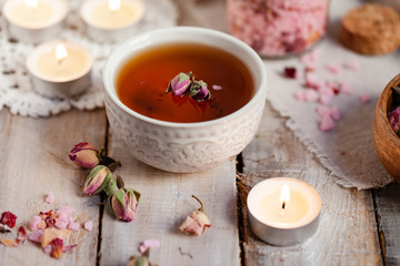 Concept of spa treatment with roses. Herbal tea, crystals of sea pink salt in bottle, candles as decor. Atmosphere of relax, anti-stress and detox procedure. Luxury lifestyle. Wooden background