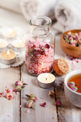 Concept of spa treatment with roses. Herbal tea, crystals of sea pink salt in bottle, candles as decor. Atmosphere of relax, anti-stress and detox procedure. Luxury lifestyle. Wooden background