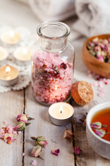 Concept of spa treatment with roses. Herbal tea, crystals of sea pink salt in bottle, candles as decor. Atmosphere of relax, anti-stress and detox procedure. Luxury lifestyle. Wooden background