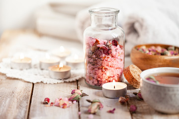 Obraz na płótnie Canvas Concept of spa treatment with roses. Crystals of sea pink salt in bottle, candles as decor. Atmosphere of relax and pleasure. Anti-stress and detox procedure. Luxury lifestyle. Wooden background