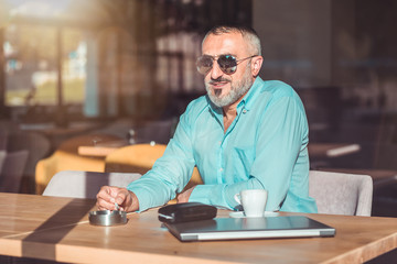 Middle aged bearded man drinking first morning coffee and smoking.