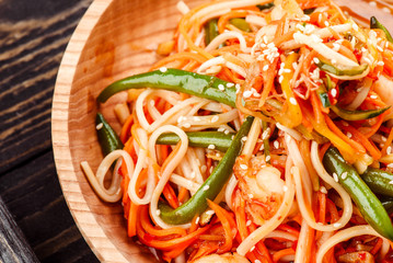 Pan-Asian food. Noodles with vegetables and asparagus beans in beautiful wooden plate on dark rustic tray on light concrete background. Beautiful composition. Close-up. Space