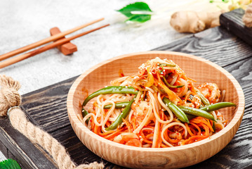 Pan-Asian food. Noodles with vegetables and asparagus beans in beautiful wooden plate on dark rustic tray on light concrete background. Beautiful composition. Close-up. Space