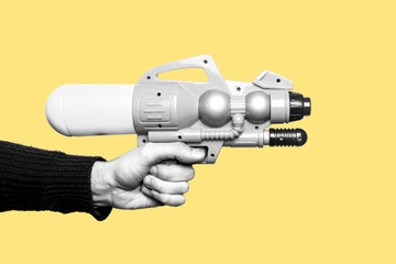 Concept of childhood, don't want to grow up, play with kids, play like a child. Hand of a young man holding a toy gun in black and white. Yellow background