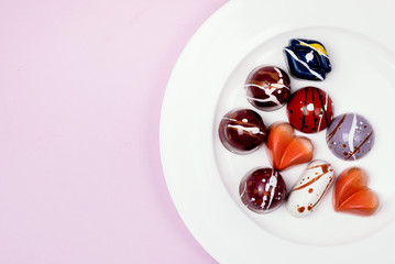 Luxury Bonbons Painted with Differents Colors on White Plate on Pink background Beautiful and Exclusive Handmade Chocolate Candy