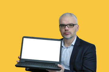 handsome man in glasses and with a beard holds a laptop with a blank screen on. Isolated on a yellow background.