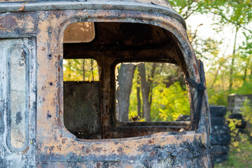 An old rusty bus with broken windows stands in a forest. Bunker at the tactical paintball playground. Closeup view