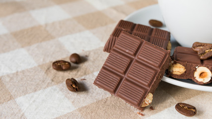 pieces of chocolate with hazelnuts and coffee beans on a brown tablecloth