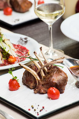 Fresh grilled veal ribs with tomatoes and sauce on a white plate on a table in a restaurant. Delicious meaty gourmet dinner. Close-up. Space