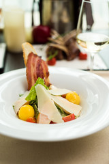 Traditional Caesar salad with chicken breast, tomatoes, lettuce, egg, parmesan and croutons in a white plate and a glass of white wine on a table in a restaurant. Close-up