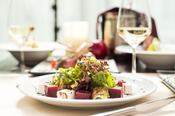 Fresh vegan salad with arugula, lettuce, beetroot, cheese and sauce on a white plate on a table in a restaurant. Close-up. Space