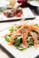 Vegetable salad with salmon, spinach and lettuce on a plate on a table in a restaurant. Glass of white wine on the background. Top view with copy space.