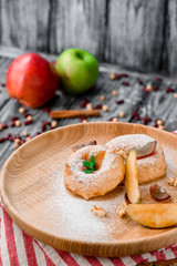 Apple donuts decorated with mint on round wooden plate on red striped napkin on gray wooden background