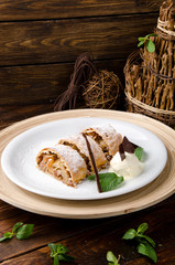 Apple strudel with creamy ice cream, garnished with mint on a white plate on a short wooden background